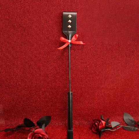 Classic BDSM whip with leather tip, metal studs and red bow on red background