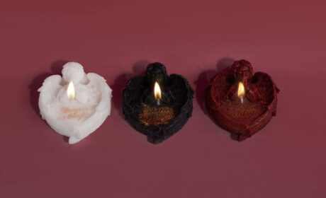 Three gothic angel candles burning in black, red, and white on a dark red backdrop