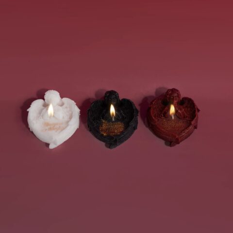 Three gothic angel candles burning in black, red, and white on a dark red backdrop